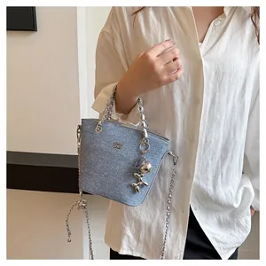 Dettaglio borsa a secchiello in denim azzurro con manico a catena e charm a palloncino