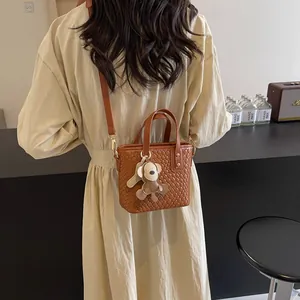 Brown woven tote bag with adjustable strap and cute bear charm shown on shoulder