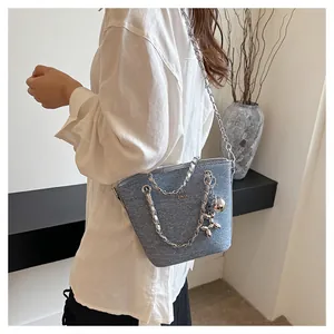 Dettaglio della borsa a secchiello in denim blu chiaro con catena e ciondolo a palloncino
