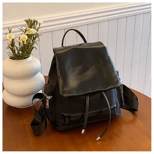 Detail of black backpack with leather flap, drawstring closure and top handle on wooden table