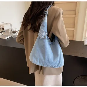 Detail of light blue denim tote bag with white rose embroidery shown on a model