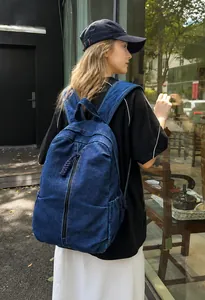 Détail du sac à dos en jean bleu foncé montrant la fermeture éclair tressée et la poche