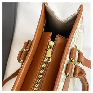 Detail view of the golden metal zipper and brown leather trim on the canvas tote bag