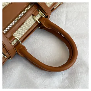 Detail of the brown leather handle and gold hardware on a beige canvas tote bag