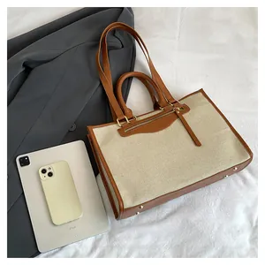 Top view of canvas tote bag with brown leather trim, tablet and blazer on fabric