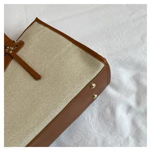 Detail view of contrast stitching, gold metal feet, and zipper on beige canvas tote bag