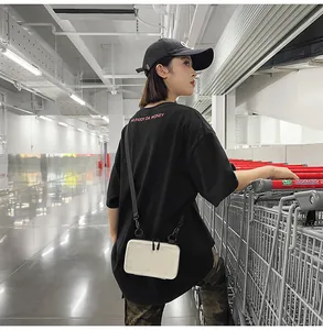 Detail view of a white hardshell mini crossbody bag and urban streetwear outfit