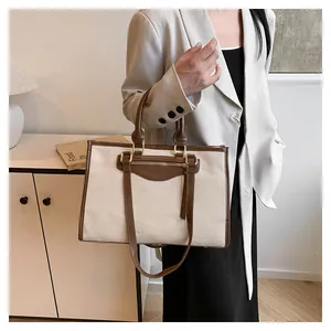 Detail of canvas tote bag with brown leather trim carried by a model in a suit