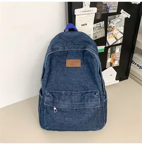 Détail d'un sac à dos en denim bleu foncé avec coutures blanches et logo en cuir