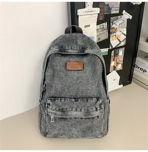 Détail d'un sac à dos vintage en jean délavé gris avec patch en cuir sur table beige