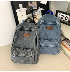 Détail de sacs à dos en denim délavé gris et bleu sur un bureau dans une ambiance scolaire