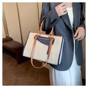 Detail of canvas tote bag showing blue leather trim, front zipper pocket and metal hardware