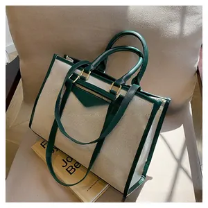 Detail of canvas tote bag with green leather trim on a beige sofa, showing textures