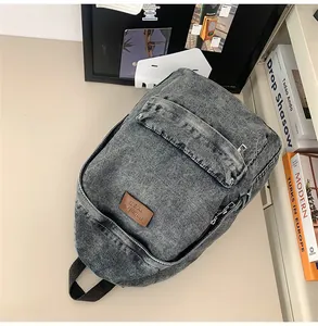 Détail macro du sac à dos en denim gris délavé avec écusson en cuir vintage