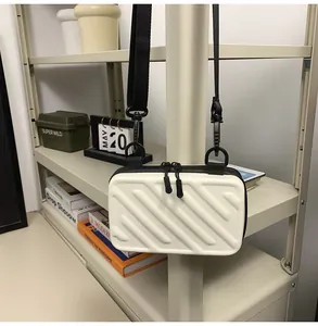 Detail of white striped hard-shell crossbody bag with dual zippers on display shelf