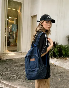 Detail view of durable navy denim backpack with brown leather patch and zip pocket