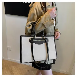 Detail of canvas tote bag showing black leather handles and golden metal hardware