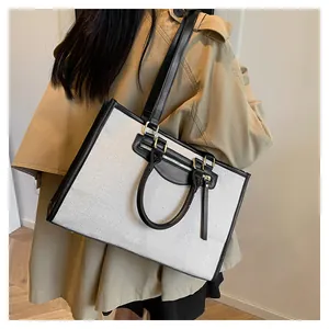 On-shoulder view of the canvas tote bag with black leather trim on a beige coat model