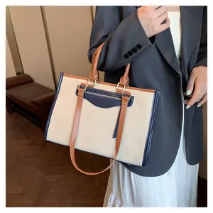 Detail of canvas tote bag showing contrast leather trim and outer zipper pocket
