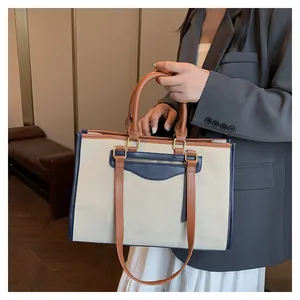 Fashionable large linen tote bag with brown leather trim worn by model in gray suit