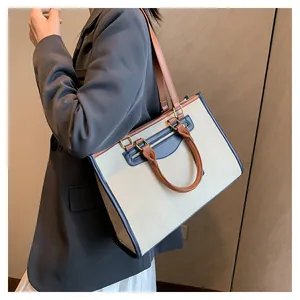Woman in grey blazer carrying a beige canvas tote with brown leather trim and blue accents