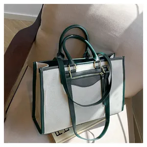 Detailed shot of beige canvas tote bag with green leather trim and dual handles on a sofa