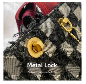 Detail of golden metal lock on grey plaid denim tote bag with red textured strap