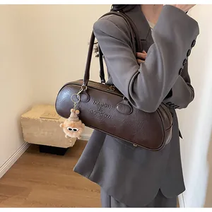Detail of vintage brown cylinder shoulder bag with embossed logo and plush toy charm