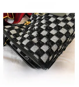 Detail of checkered denim tote featuring fringe edges and red-black striped strap