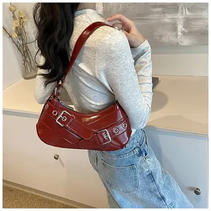 Detail of dark red patent leather underarm bag with silver buckles and metal eyelets