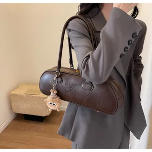 Macro detail of dark brown baguette shoulder bag with embossed logo and plush bear charm