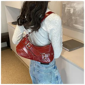 Detail of dark red patent leather shoulder bag with metallic eyelets and buckle straps