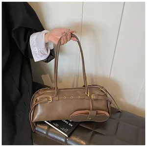 Macro detail of brown leather baguette bag with metal eyelets and mini pouch charm