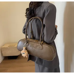 Close-up of brown textured leather cylinder bag with logo and cute plush charm detail