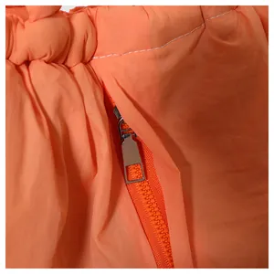Detail of glossy orange puffer bag fabric with metal zipper and precise white stitching