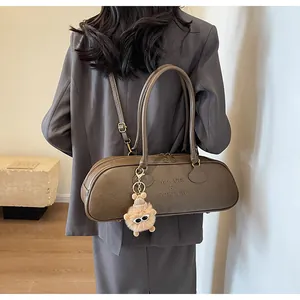 Detail of dark brown vintage cylinder shoulder bag with plush monster charm and brand embossing