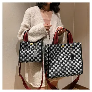Detail of checkered denim tote bag featuring red woven handles and golden twist lock