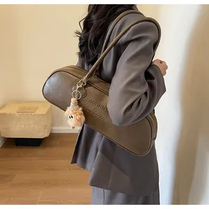 Detail of a brown cylindrical baguette bag featuring embossed letters and a plush charm