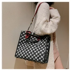 Detail of checkered denim tote with fringe edges and red woven handle accents