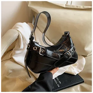 Close-up of black glossy baguette bag with silver metallic buckles and eyelet details