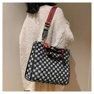 Detail of checkered denim tote bag featuring fringed edges and a contrast red shoulder strap