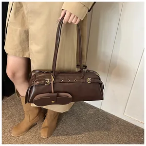 Detail of burgundy leather baguette bag with metal buckles on shoulder strap worn with coat