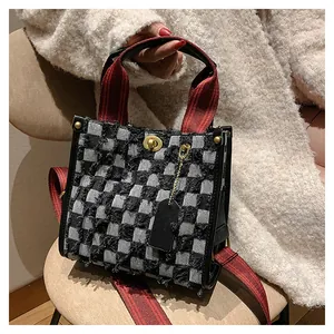 Detail of checkered tote bag with red handles, gold metal twist lock, and frayed edges