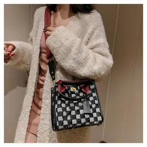 Detailed close-up of a checkered tote bag with a gold twist lock and a red shoulder strap