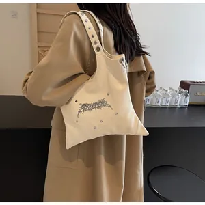 Dettaglio della borsa a tracolla in pelle crema con logo gotico e rivetti in metallo argento