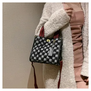 Close-up of checkered denim tote featuring red handles and golden metal twist-lock buckle