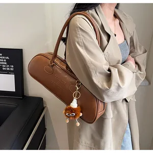 Detail of a brown leather bag with side branding and a plush doll keychain on the zipper
