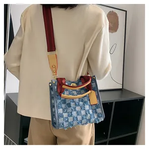 Detail of checkered denim tote with fringe edges, yellow leather handle and gold twist lock
