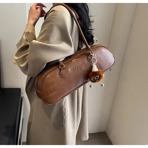 Close-up of brown vintage leather baguette bag with logo embossing and plush charm