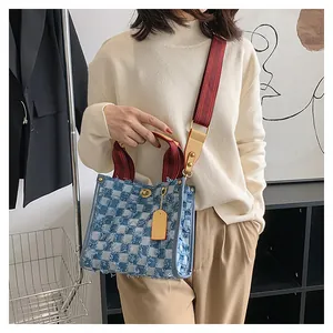 Detail of blue checkerboard denim tote bag with frayed edges and striped shoulder strap